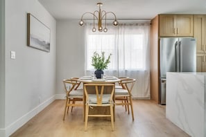 A dining area with a round table, six chairs, a chandelier, a potted plant, and a kitchen with a refrigerator. - Vegas 3BR Pool Retreat · Sleeps 10 · Putting Green · Shuffleboard (Las Vegas)