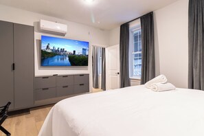 Quarto de hotel com cama, televisão fixada na parede, guarda-roupa e janela com cortinas.