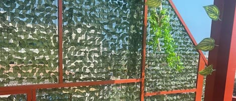 Um quarto com estrutura de metal vermelha, um banco de madeira e uma parede coberta por folhagem verde.