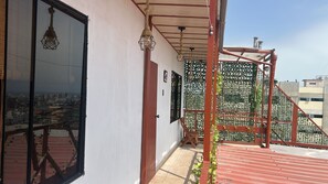 Un balcón con vistas a un paisaje urbano, una silla de madera y una barandilla de metal.