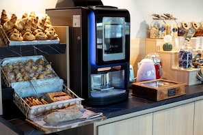 Una estación de café con una cafetera, pasteles y pan.