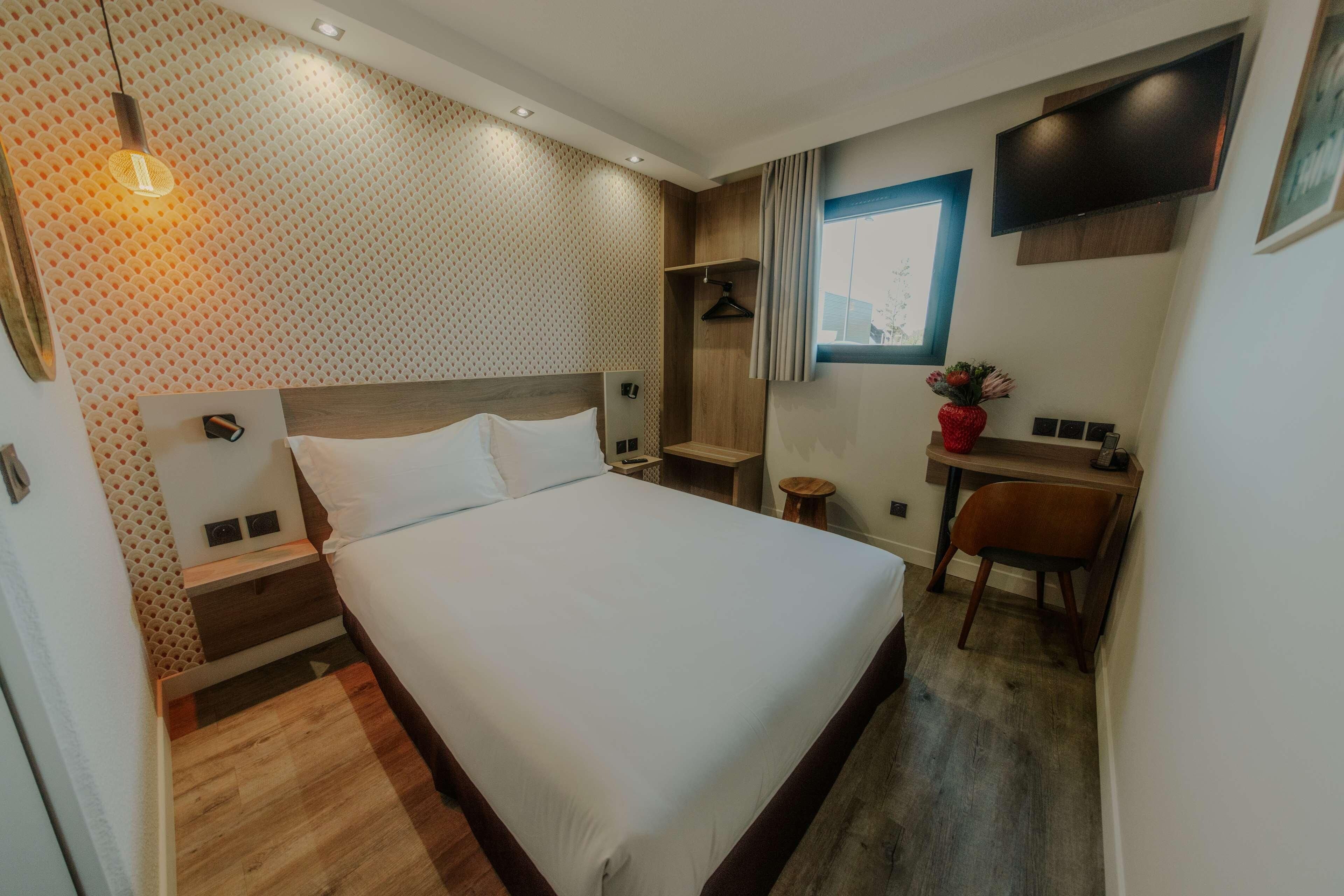 A modern hotel room with a large bed, bedside tables, a desk, and a TV mounted on the wall.