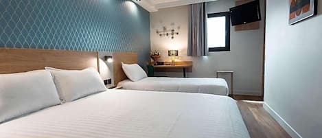 A hotel room with two beds, a desk, a TV, and a window.