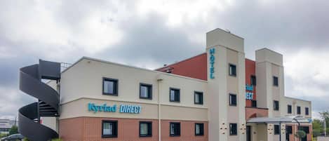 A hotel named 'Kyriad DIRECT' with a modern design, featuring a prominent spiral staircase and a swimming pool.