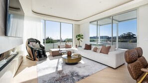 Un salon moderne comprenant un canapé, une table basse et un fauteuil massant, ainsi que de grandes fenêtres donnant sur l’extérieur.