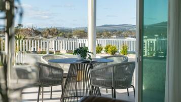 A balcony with a round table and four chairs, a potted plant, and a view of a bridge and landscape.