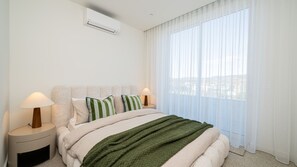 Une chambre d’hôtel avec un lit, deux lampes de chevet, une fenêtre avec des rideaux légers et un climatiseur fixé au mur.