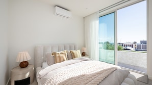 Une chambre moderne avec un grand lit, des lampes de chevet, une fenêtre donnant sur la ville et un appareil de climatisation.