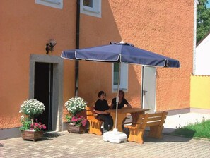 Een buitenruimte met een tafel en stoelen, een bank en een grote parasol voor schaduw.