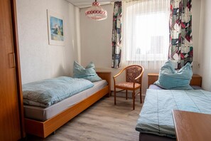 Een slaapkamer met twee enkele bedden, een houten bureau, een stoel en een raam met gordijnen.