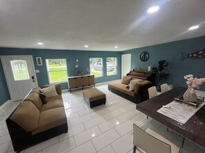 A living room with a sofa, ottoman, dining table, and piano. - Cozy 1-bedroom in beautiful Clute with AC (Clute)