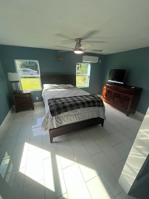 A bedroom with a bed, a ceiling fan, a TV, and two windows.