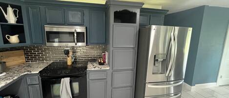 Una cocina con gabinetes grises, un refrigerador de acero inoxidable, un microondas y una estufa.