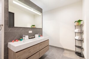 A modern bathroom with a large mirror, a double sink vanity, and a towel rack. - Apartment - Perla di Cape Marie 1412 (Jan Kok)