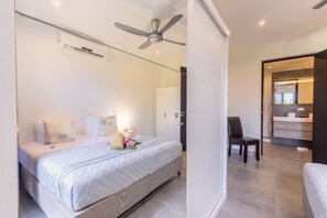 A modern bedroom with a bed, bedside tables, a ceiling fan, and an air conditioning unit. - Apartment - Perla di Cape Marie 1412 (Jan Kok)