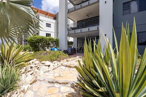 A courtyard with a stone pathway, a dining area, and a building with balconies. - Ground-Floor 2BR Condo · Pool steps away · Curaçao (Jan Kok)