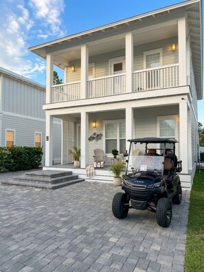A two-story house with a covered porch, a golf cart parked in front, and a paved driveway. - NEW! Walk to Beach, HotTub, Heated Pool, 6-Seat Golf Cart, Games (Santa Rosa Beach)