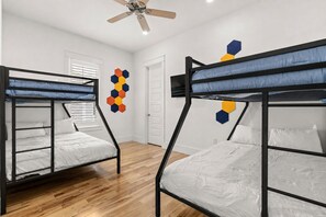 A room with bunk beds, a ceiling fan, a wooden floor, and a wall decoration. - NEW! Walk to Beach, HotTub, Heated Pool, 6-Seat Golf Cart, Games (Santa Rosa Beach)