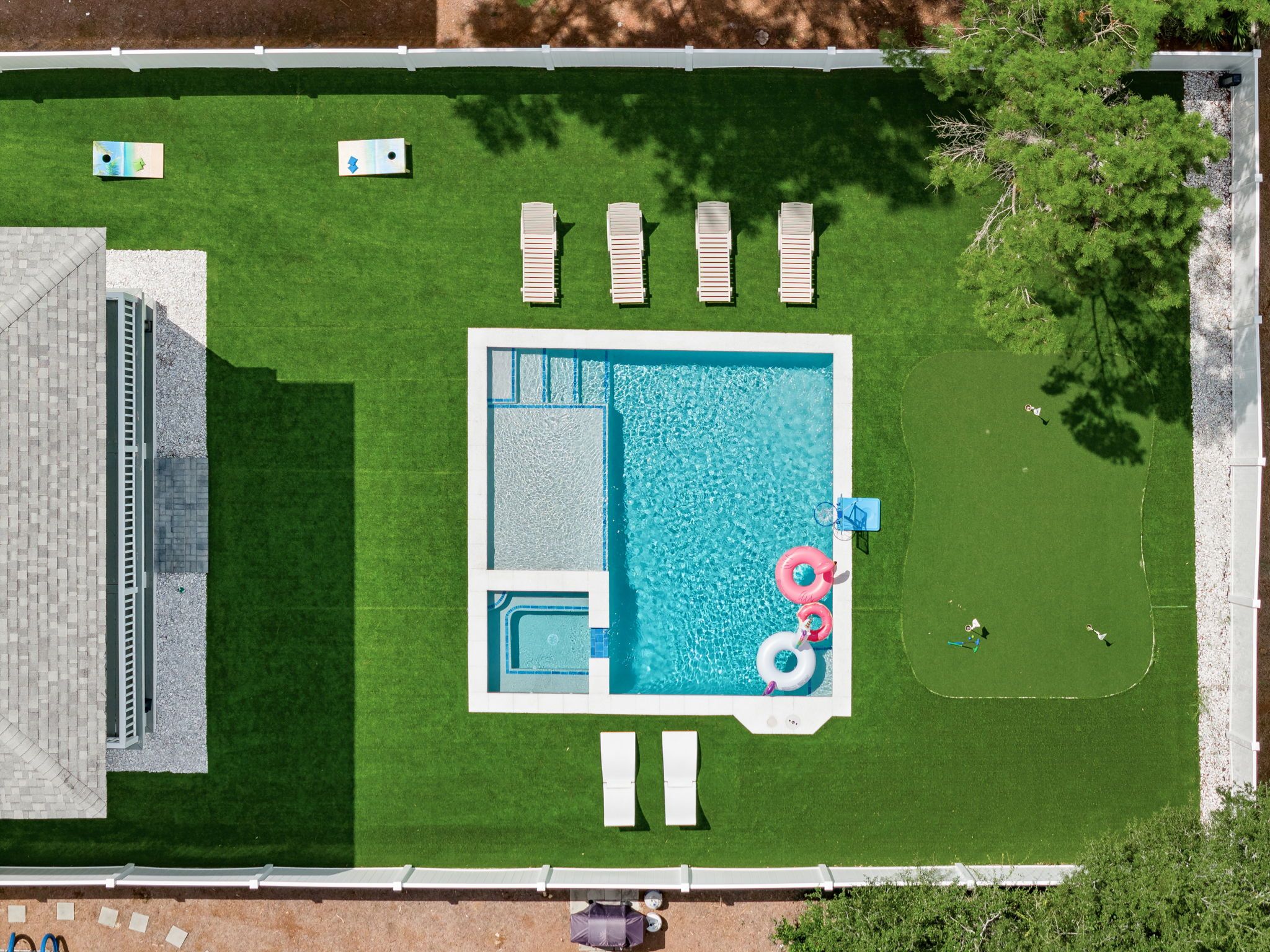 A rectangular swimming pool with a small hot tub, surrounded by a grassy deck with lounge chairs.