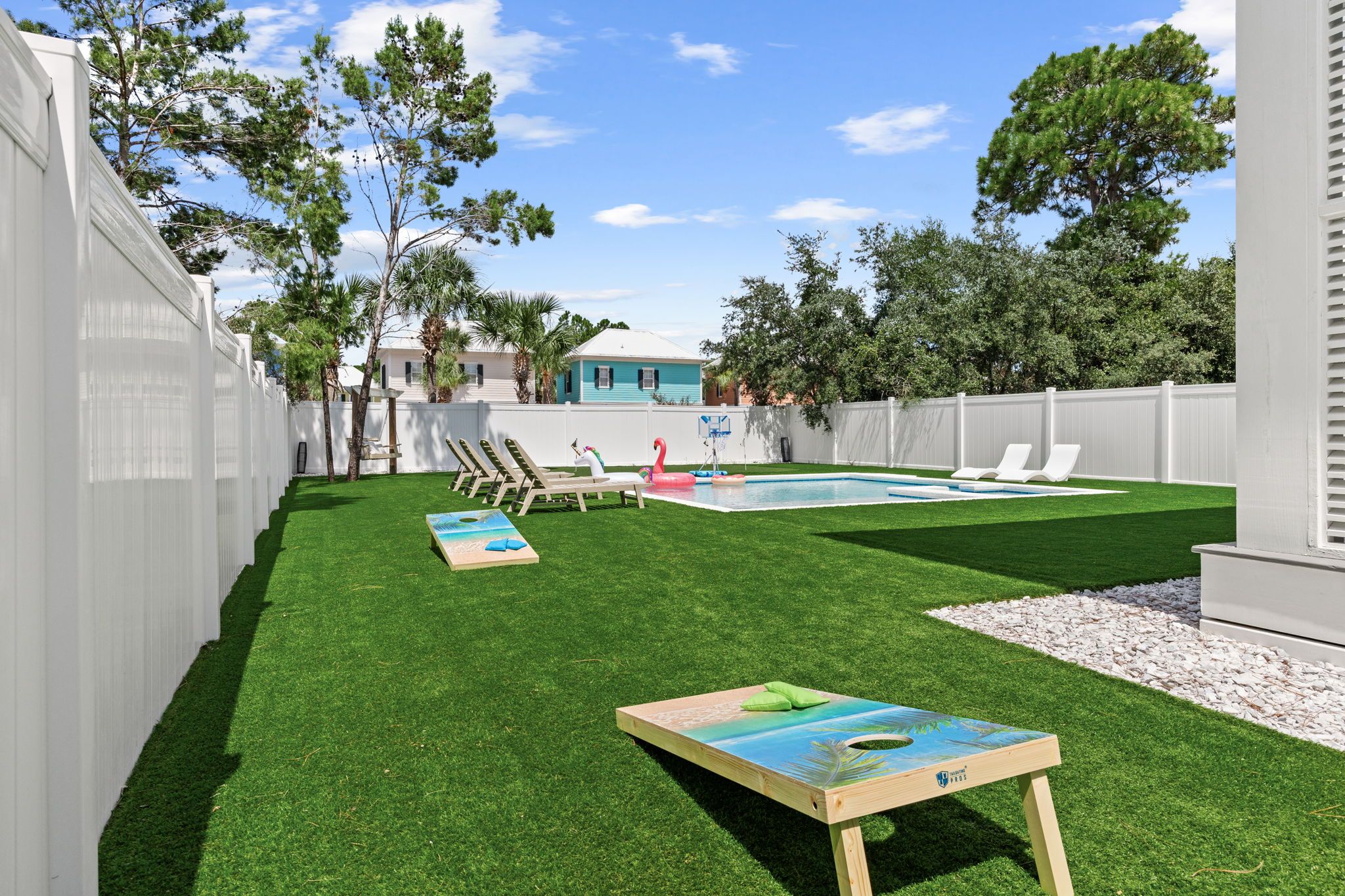 A backyard with artificial grass, a pool, lounge chairs, and a wooden deck.