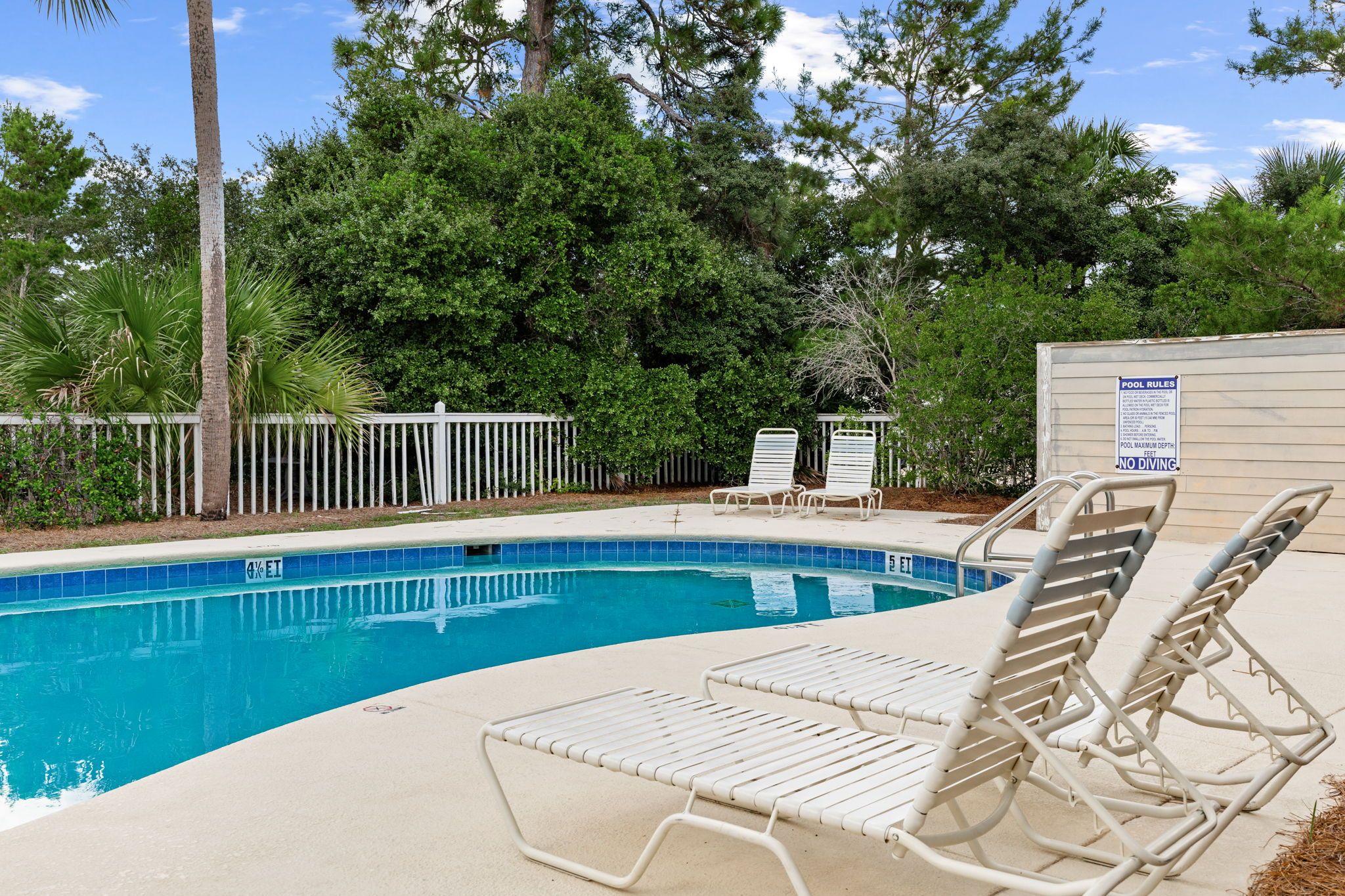 A swimming pool with lounge chairs and a fence.