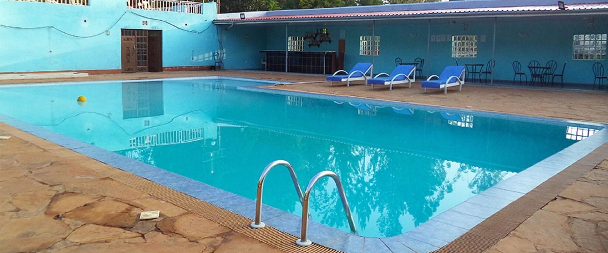 Una piscina con borde de azulejos, una escalera de metal y sillas de descanso azules.