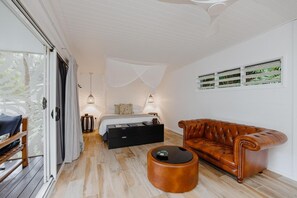 Een kamer met een bed, een leren bank, een klein rond tafeltje en een raam met jaloezieën.