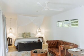 A bedroom with a bed, bedside tables, a ceiling fan, a window, and a brown leather sofa. - Mist At Cape Tribulation (Cape Tribulation)
