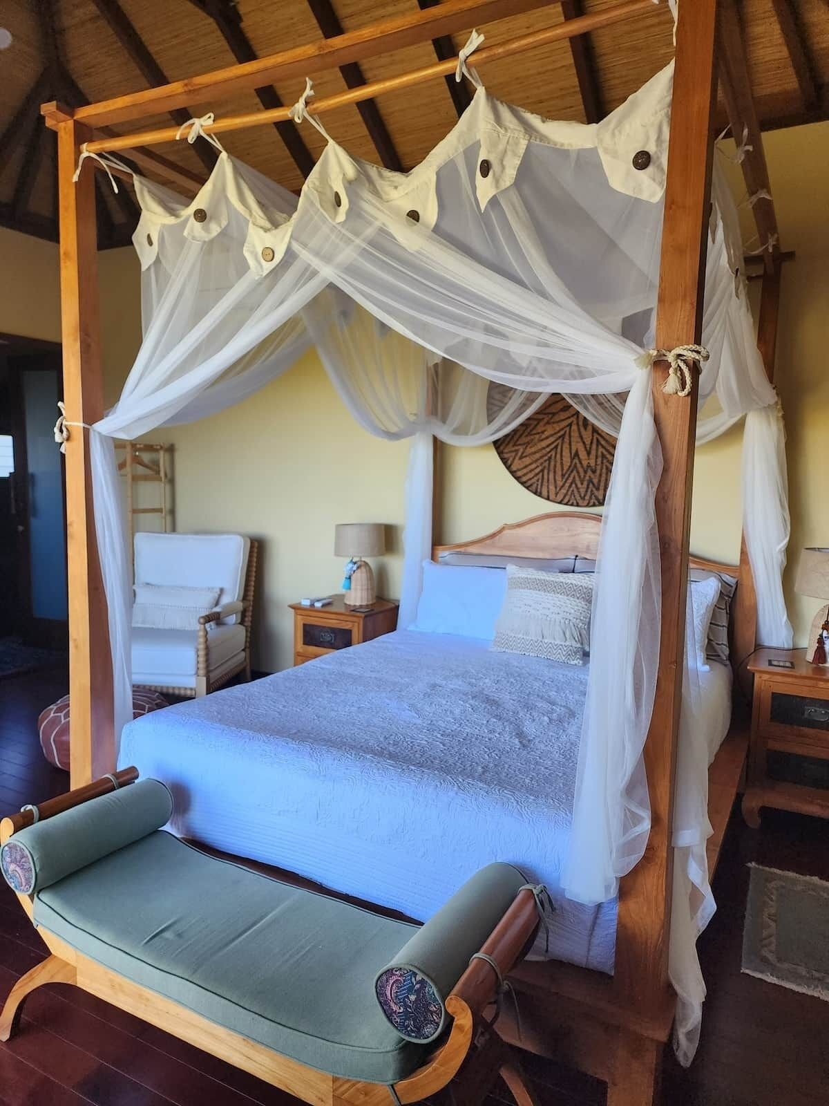 A four-poster canopy bed with a matching canopy chair, a bedside table with a lamp, and a nightstand with a lamp.