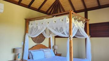 A four-poster bed with a canopy, a wooden table with chairs, and a ceiling fan.