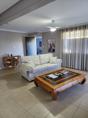 A living room with a sofa, a coffee table, a dining table with chairs, and a ceiling fan.