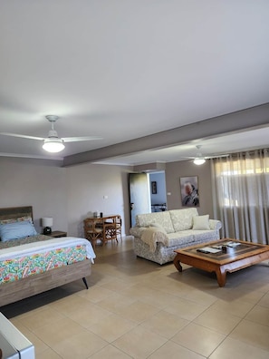Une chambre d’hôtel comprenant un lit, un canapé, une table basse, une table à manger avec des chaises et un ventilateur de plafond.