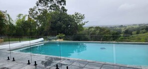 A rectangular swimming pool with a clear blue water surface, surrounded by a stone deck and a metal fence.