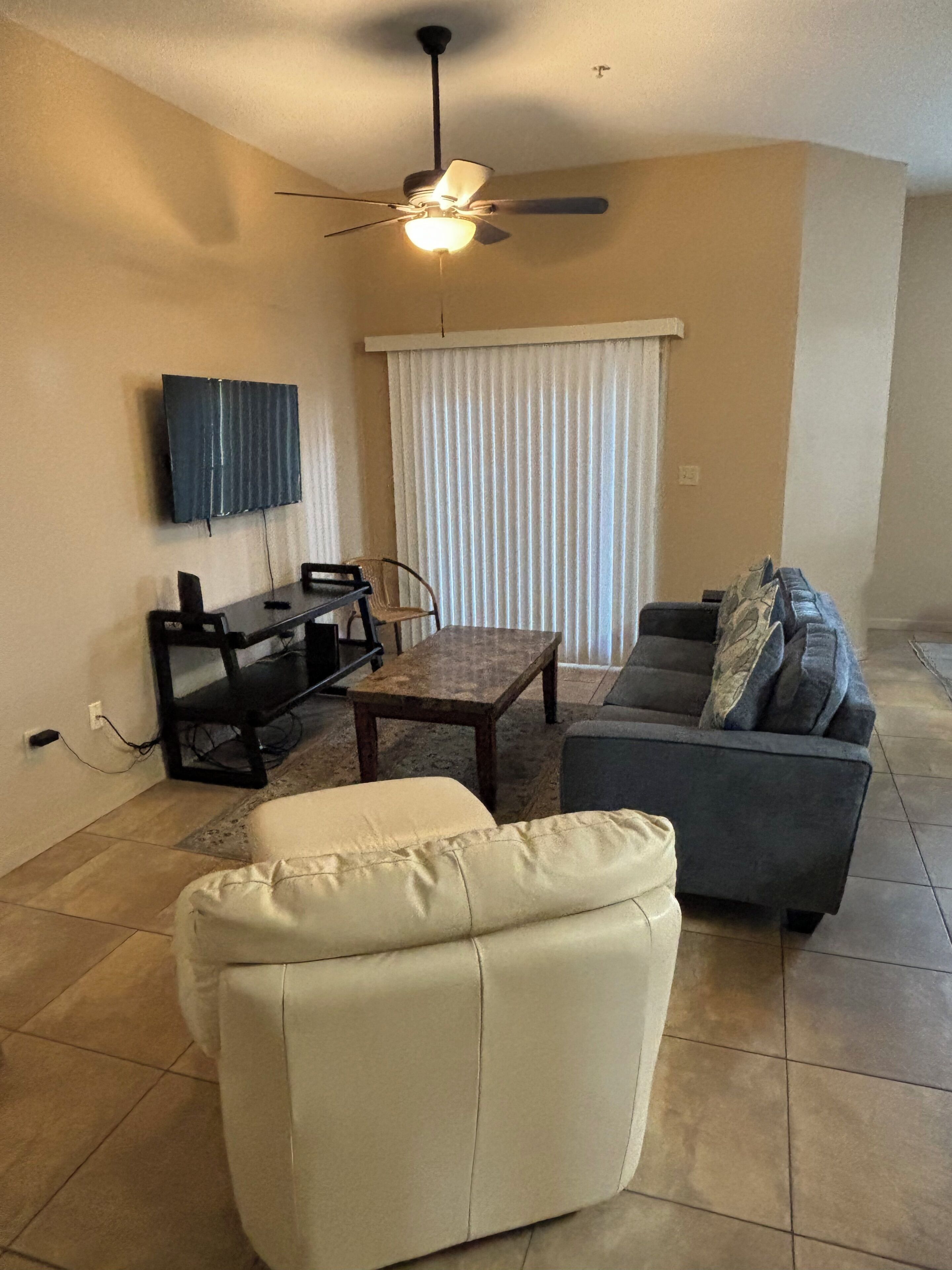 A living room with a sofa, a coffee table, a television mounted on the wall, and a ceiling fan.