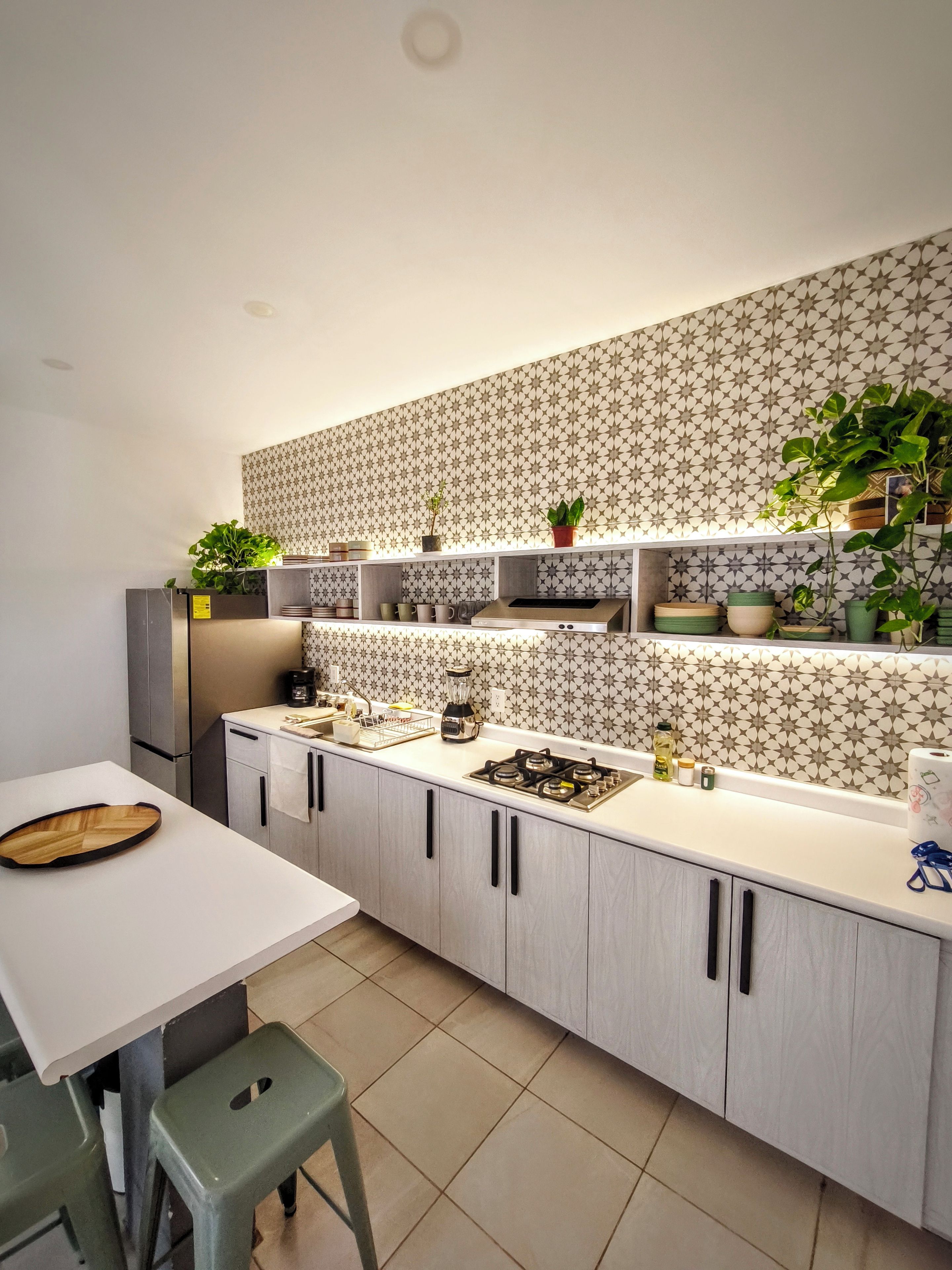 A modern kitchen with a white countertop, grey cabinets, and a patterned backsplash.