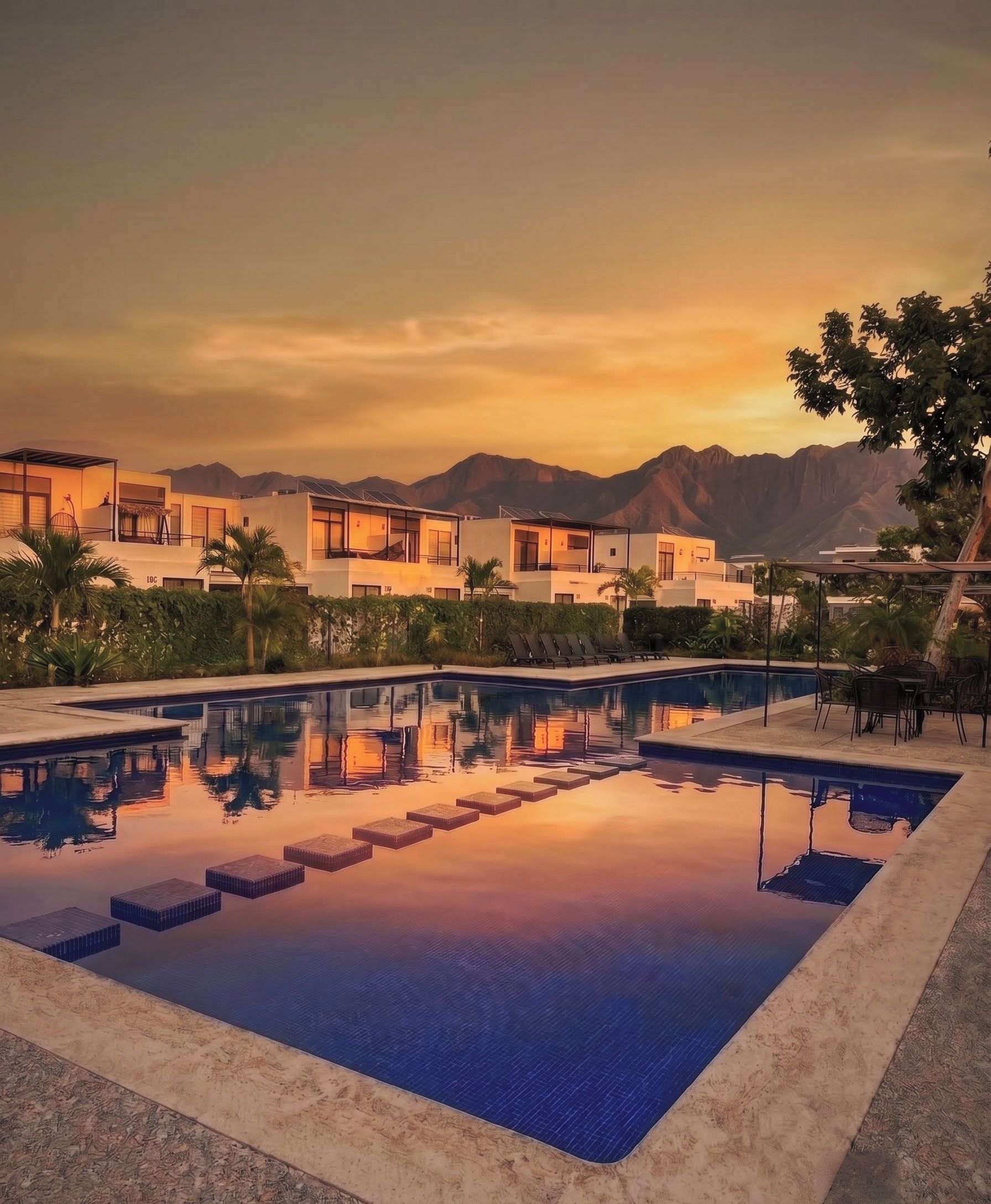 A modern resort with a swimming pool, multiple-story buildings, and a mountainous backdrop.