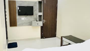 A modern bedroom with a bed, a TV mounted on the wall, a wooden wardrobe, and a small bedside table.