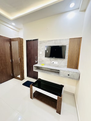 A modern living room with a flat-screen TV mounted on a marble wall, wooden wardrobe, and a black coffee table.