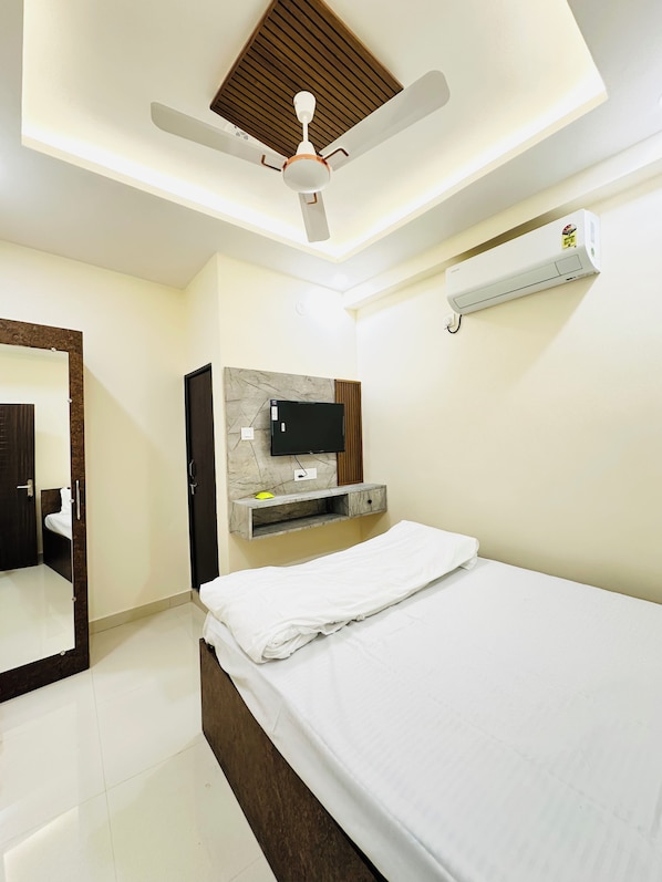 Un dormitorio con una cama, ventilador de techo, televisor montado y aire acondicionado instalado en la pared.