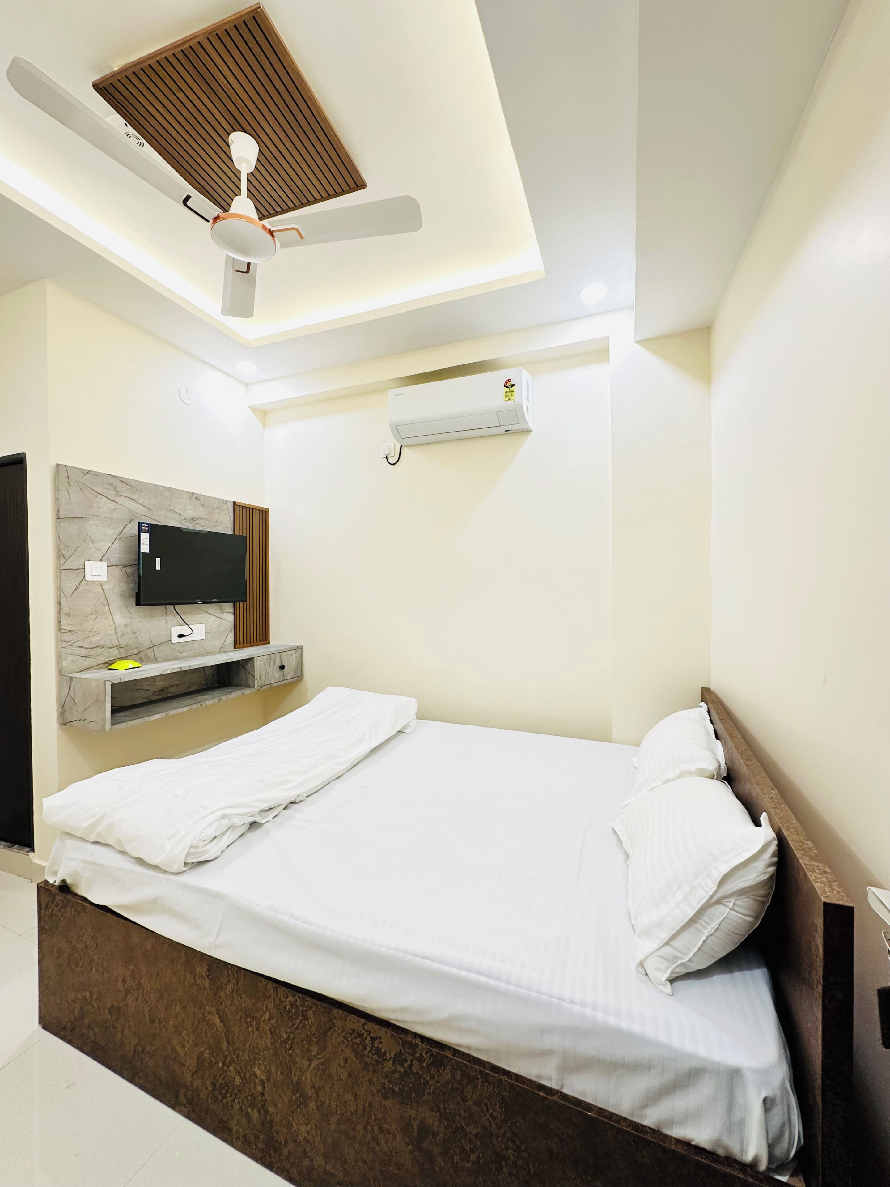 A modern bedroom with a bed, a ceiling fan, an air conditioning unit, a mounted TV, and a wooden headboard.
