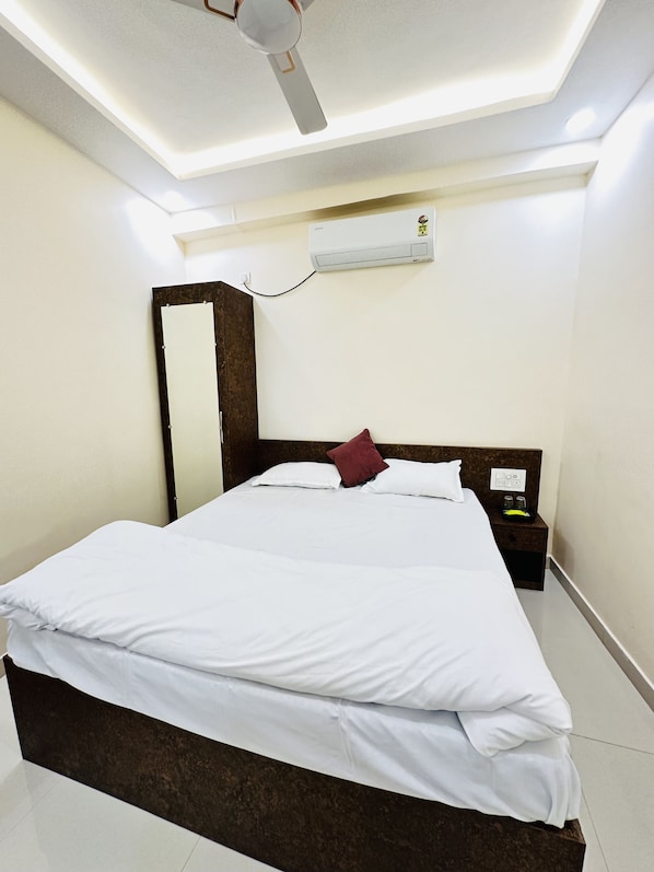 A hotel room with a bed, a nightstand, a wall-mounted air conditioner, and a ceiling fan.