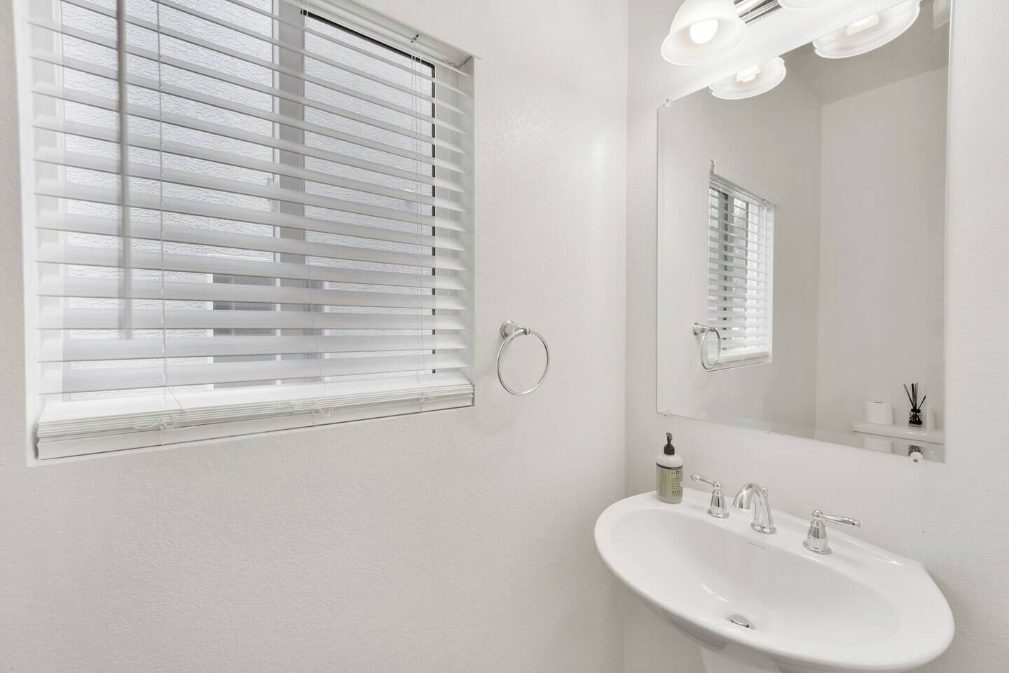 Une salle de bain avec un lavabo blanc, un miroir et une fenêtre avec des stores.