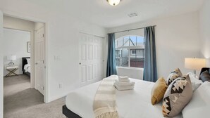 Quarto de hotel com cama, mesa de cabeceira, luminária, janela com cortinas e vista para o exterior.