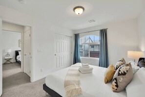 Habitación de hotel con cama, mesita de noche, lámpara, ventana con cortinas y vista al exterior.