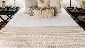 Ein Bett mit einer beigen Decke, mehreren Kissen und zwei Nachttischen mit Dekoration.
