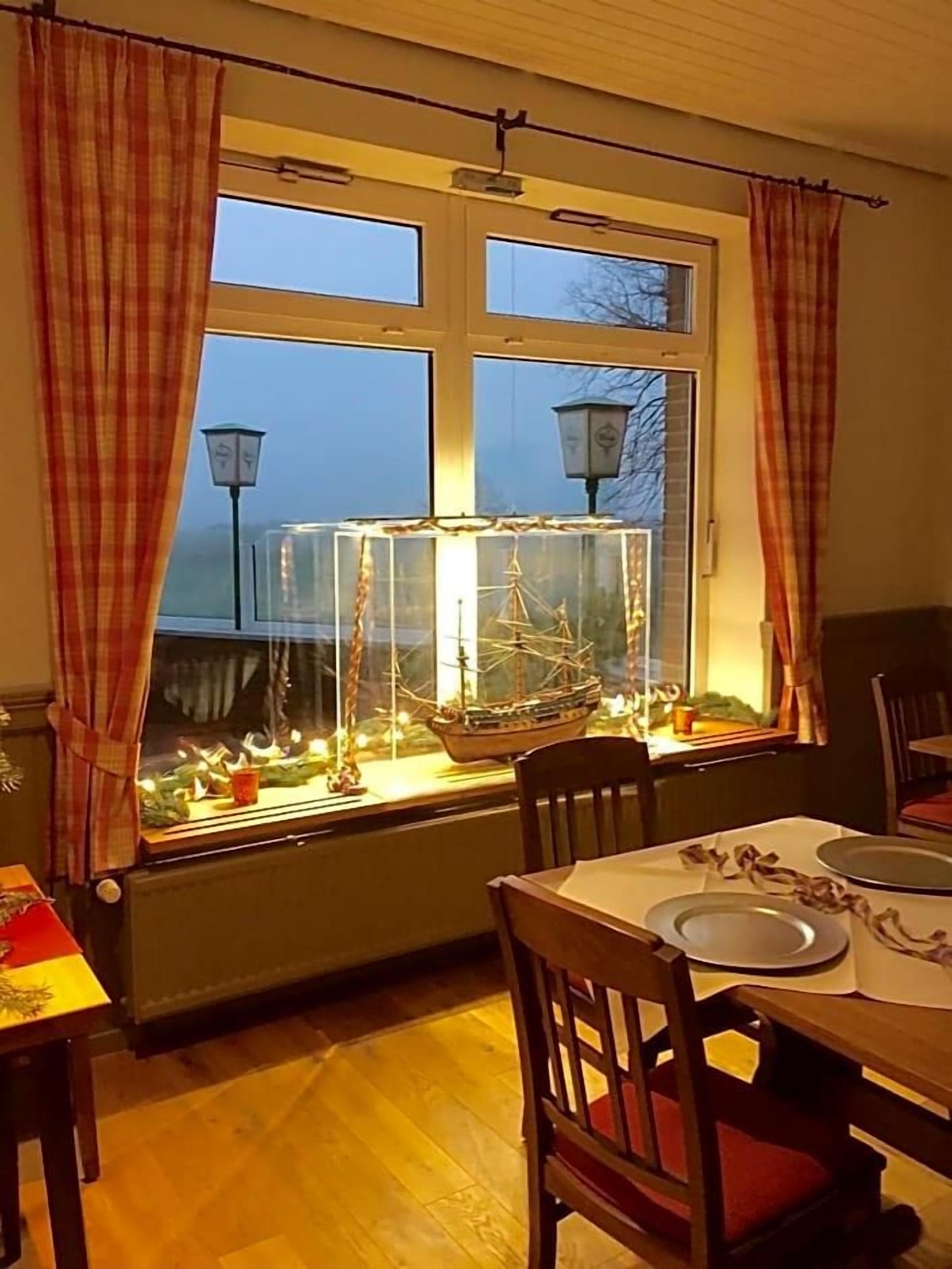 Ein Essbereich mit einem Tisch für zwei Personen, einem Fenster mit Vorhängen und einem dekorativen Schiffsmodell in einer Vitrine.