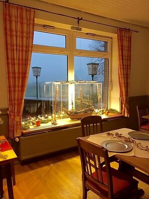 A dining area with a table set for two, a window with curtains, and a decorative ship model inside a glass case. - Landgasthof Waabs Mvºhle (Waabs)