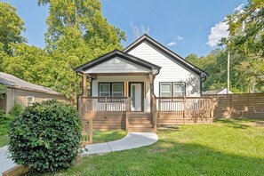 Ein eingeschossiges Haus mit Veranda, einem eingezäunten Garten und einem kleinen Busch im Vordergrund.