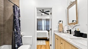 Ein modernes Badezimmer mit Badewanne, Toilette, Duschvorhang und Waschtisch mit Spiegel und Spüle.