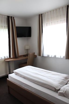 A hotel room with a bed, a desk, a chair, a TV, and curtains. - Pension Buongusto (Steinmauern)